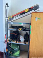 Overall view of shelving with boxed lawn edging, pole tools, blower, sprayer, tool bag and hand tools