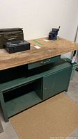 Full view of green metal workbench with wood top, drawer, shelf, cabinet