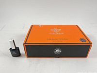 Closed orange/black Modelones box beside one bottle