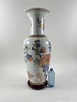 Full view of vase on base beside water bottle for scale