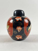 Front view of ginger jar showing black panels with red borders and lotus flowers