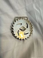 Front view of circular silver-tone saw blade edge belt buckle