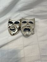 front view of silver-tone belt buckle showing comedy and tragedy masks with black enamel