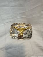 Front view showing gold-tone longhorn head on silver-tone patterned background