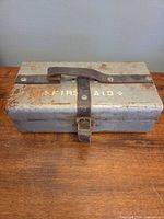 Closed metal first aid box showing exterior, leather strap, rust and stencilled lettering