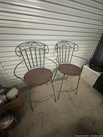 Both tall wrought iron garden chairs leaning against storage unit door