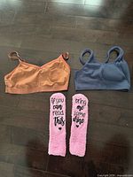 Overview of two sports bras and pair of pink novelty socks laid on dark wood floor