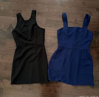 Front view of both dresses laid flat: black sheath and navy dress with pockets