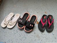 Three sandal pairs lined up: white flip flops, Under Armour slides, Okabashi thongs