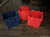 Front view of three fabric storage bins, upright, showing colors and handles