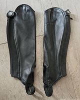 Front view of both black synthetic half chaps showing overall condition, zippers, snaps, and foot straps