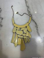 Full view of cream geometric bib necklace on marble surface