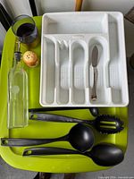 All items laid out on green surface: cutlery holder, oil bottle, three black utensils, knife, salt shaker, tumbler