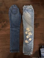 Both pairs of jeans laid flat, dark blue pair left, light blue floral pair right