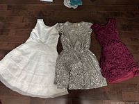 Front view of three dresses laid out: white, silver sequin, burgundy lace