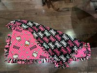 Full view of both sides of the double-sided Hello Kitty fleece blanket displaying patterns and knotted fringe