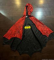 Cape laid flat showing red web side with hood and inner black Batman logo side