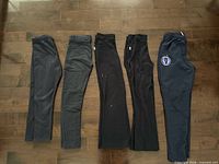 Five pairs dark uniform pants laid flat side by side