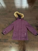Front view of purple Ripzone kids winter coat with faux fur hood, pockets visible