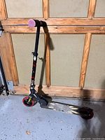 Full view of folding kick scooter leaning against garage door