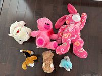 Top view of six assorted plush stuffed animals on dark floor