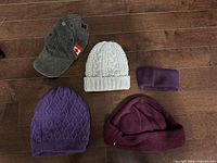 All five pieces laid out: ear-flap cap, two knit beanies, cuffed beanie, fleece headband