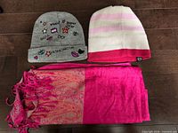 Two kids’ knit beanies and a bright pink woven scarf laid flat on floor