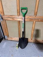 Full view of shovel standing against wall, showing blade, shaft label, and D-handle