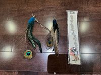 Two peacock feather earrings and one packaged rhinestone hair band on wooden surface
