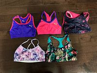 Five assorted teen sports bras arranged on floor