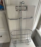 Front view of chrome toilet paper holder showing arms, basket and hanger