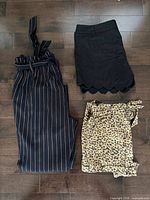 Overview of three garments laid out: pinstripe trousers, black scallop shorts, leopard wrap shorts