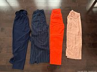 Four clothing items laid flat: navy pants, pinstripe pants, orange pants, blush skirt