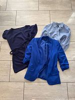 Three garments laid out: navy dress, royal blue blazer, light blue shirt