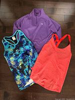 Three women’s workout tops laid flat: purple quarter-zip, coral racerback, blue patterned racerback