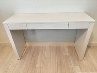 Front view of white high-gloss desk showing drawer and panel legs