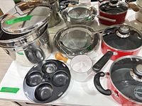 Overview of stainless pot, strainers, red saucepan, egg poacher, assorted pieces