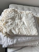 Folded cream throw on top of white quilted coverlet