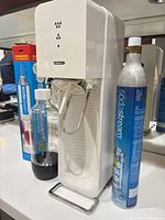 Front angle showing white SodaStream carbonator, loose CO2 cylinder and 1 L bottle
