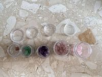 Top view of sample jars, five filled with assorted gemstones, three lids above