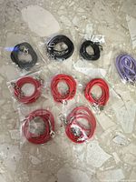 Nine necklace cords in individual plastic sleeves sorted by color on stone surface