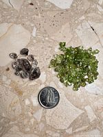 Pile of smoky quartz pieces beside larger pile of peridot chips with coin for scale