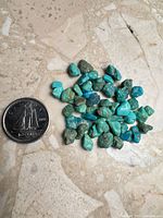 Pile of assorted raw turquoise stones next to a Canadian quarter for scale