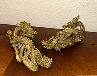 Two brass dragon figurines side view on wood surface