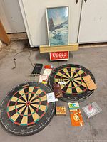 Lot overview showing two dartboards, Coors sign, dart sets, puzzles