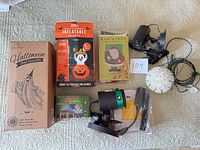 All boxed and loose items laid out: laser projector, snowflake projector, inflatable box, ghost decoration box, flag, icicle lights box, hanging light ball