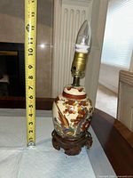 Front view of porcelain lamp showing pheasant floral design, wood stand, bulb and measuring tape