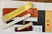 Overview of three slide rules with their cases and booklet on table