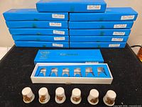 Stack of 12 blue Keepsakes boxes with one open tray showing six thimbles; seven thimbles displayed in front
