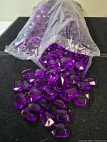 Bag opened showing numerous purple faceted acrylic gems spilling out
